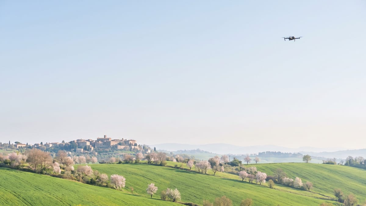 Collina italiana in primavera con campi verdi e un piccolo drone in volo sulla destra
