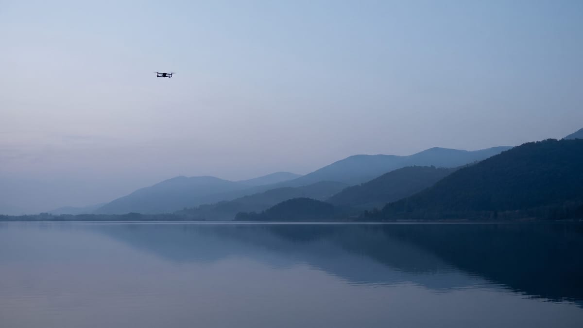Lago italiano all'alba con colline in strati successivi e un piccolo drone in volo sulla sinistra